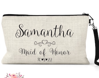 May include: A beige linen makeup bag with a black zipper and a black strap. The bag has the text "Samantha Maid of Honor 10-8-22" printed on it.