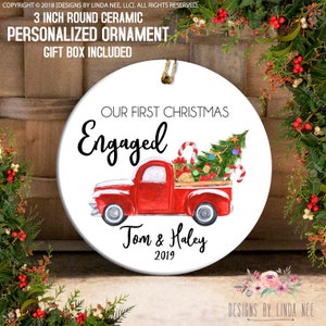 Puede incluir: Un adorno de cerámica blanco con un camión rojo que lleva un árbol de Navidad, bastones de caramelo y regalos. El adorno dice "Our First Christmas Engaged Tom & Haley 2019".