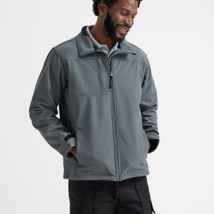 Può includere: Una giacca softshell grigio ardesia con cerniera frontale, colletto alto e maniche lunghe con polsini regolabili. La giacca presenta una tasca verticale sul petto con cerniera e due tasche laterali, indossata sopra una camicia grigio chiaro.