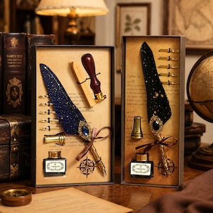 May include: Two rectangular gift boxes containing calligraphy sets. Each set includes a quill pen with a gold-tone metal tip and a decorative jewel, a glass ink bottle, a metal pen stand, and multiple nibs. One quill is dark blue with gold speckles, the other is black with gold speckles.