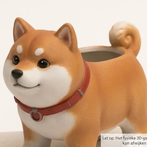 Puede incluir: Una maceta con forma de perro Shiba Inu de pelaje marrón y blanco, con un collar rojo y un pequeño anillo. El perro tiene la cola enroscada y una abertura hueca en el lomo. El texto en la imagen dice: Let op: Het fysieke 3D-geprinte model kan afwijken van de foto.