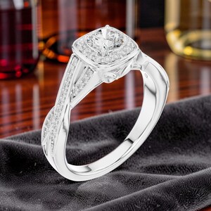 Può includere: Un anello color argento con una pietra centrale rotonda circondata da un alone quadrato di pietre più piccole. La fascia presenta un design a gambo diviso con pietre incastonate a pavé lungo i lati e una finitura metallica lucida.