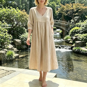 May include: A beige midi-length dress featuring a V-neckline, three-quarter length sleeves, and vertical lace trim detailing along the bodice. The garment has a gathered waistline and a loose, flowing skirt that falls below the knees.