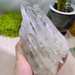 May include: A large cluster of clear quartz crystals featuring multiple elongated, pointed terminations with translucent to transparent facets. The mineral formation displays natural striations and internal inclusions throughout the structure.