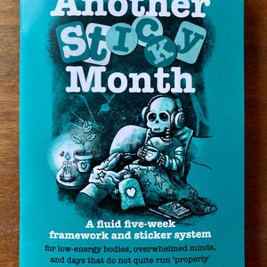 May include: A teal book cover with the title "Another Sticky Month" in white and teal lettering. The illustration shows a skeleton wearing headphones, holding a mug, and sitting on a couch. The text at the bottom describes a five-week framework and sticker system.