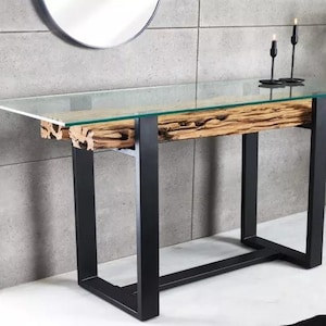 May include: A contemporary console table featuring a clear glass top and a natural wood base. The base is supported by black metal legs. Two black candle holders sit on the table. The table is 152 cm long.