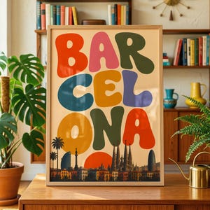 Puede incluir: Una lámina decorativa rectangular enmarcada con la palabra BARCELONA en letras grandes, coloridas y redondeadas. Debajo del texto aparece una silueta detallada del horizonte de Barcelona, incluida la Sagrada Familia, sobre un fondo crema.