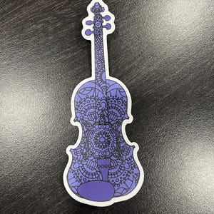 Puede incluir: Una pegatina de violín con estampado morado y negro. El violín está contorneado en negro y relleno con un diseño de mandala morado.