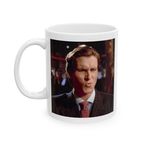 Puede incluir: Taza de cerámica blanca con una imagen en color de un hombre con traje y corbata. El hombre está haciendo una expresión facial. La taza tiene un asa blanca y un interior blanco.