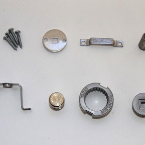 May include: Assortment of silver-toned metal parts for a coffee grinder, including screws, a spring, a metal plate with a square hole, a metal plate with a gear, a metal plate with a square hole, and a metal bracket.