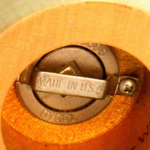 May include: Close-up of a wooden pepper mill with a metal grinding mechanism. The mechanism is labeled "Made in U.S.A. Steel".