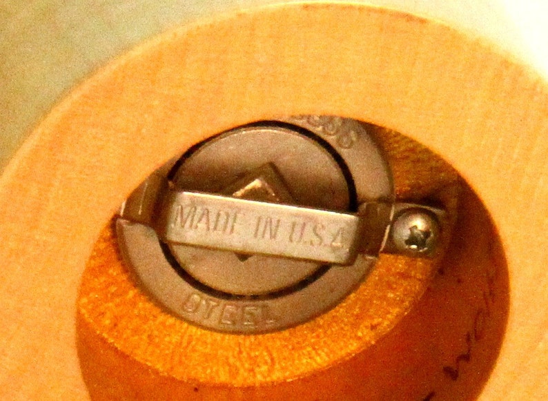 May include: Close-up of a wooden pepper mill with a metal grinding mechanism. The mechanism is labeled "Made in U.S.A. Steel".