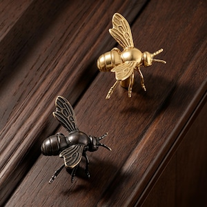 Può includere: Due pomelli per mobile a forma di ape, uno con finitura color oro lucido e l'altro con finitura color bronzo antico scuro. Ogni pomello presenta ali dettagliate, un corpo segmentato e antenne, progettati per fungere da maniglia decorativa.