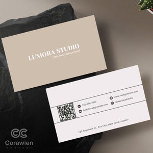 May include: Two rectangular business cards. The top card is beige with white text reading LUMORA STUDIO CREATIVE CONSULTANT. The bottom card is white with black text, a QR code, phone number 123-456-7890, email hello@reallygreatsite.com, website, and address.