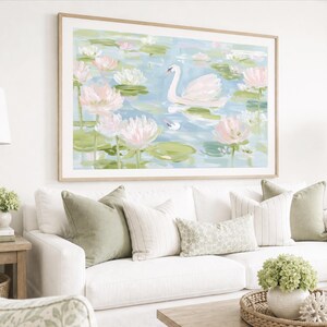May include: A large rectangular wall art print in a light wood frame featuring an impressionistic painting of a white swan swimming in a pond filled with pink water lilies and green lily pads, set against a soft blue and white water background.