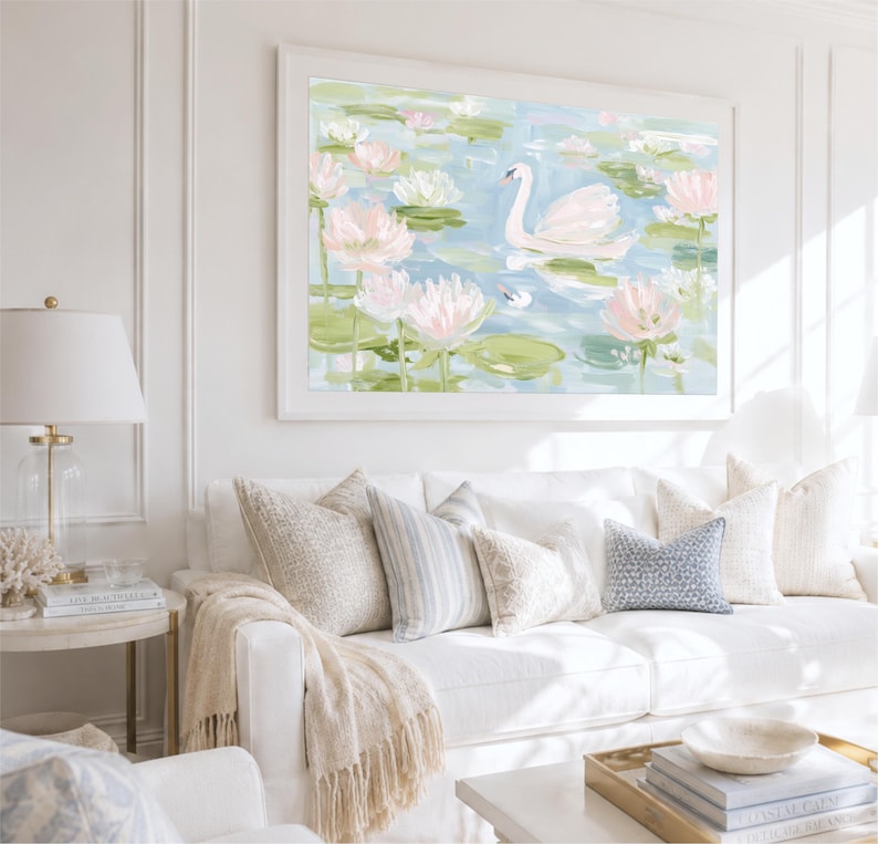 May include: A framed wall art print featuring a white swan swimming in a pond filled with light pink lotus flowers and green lily pads. The painting uses soft brushstrokes in shades of blue, white, and pink to depict a serene water scene.