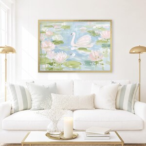 May include: A rectangular wall art print in a gold frame featuring an impressionistic painting of a white swan swimming in a pond filled with light pink lotus flowers and green lily pads, rendered in soft pastel blue, green, and pink tones.