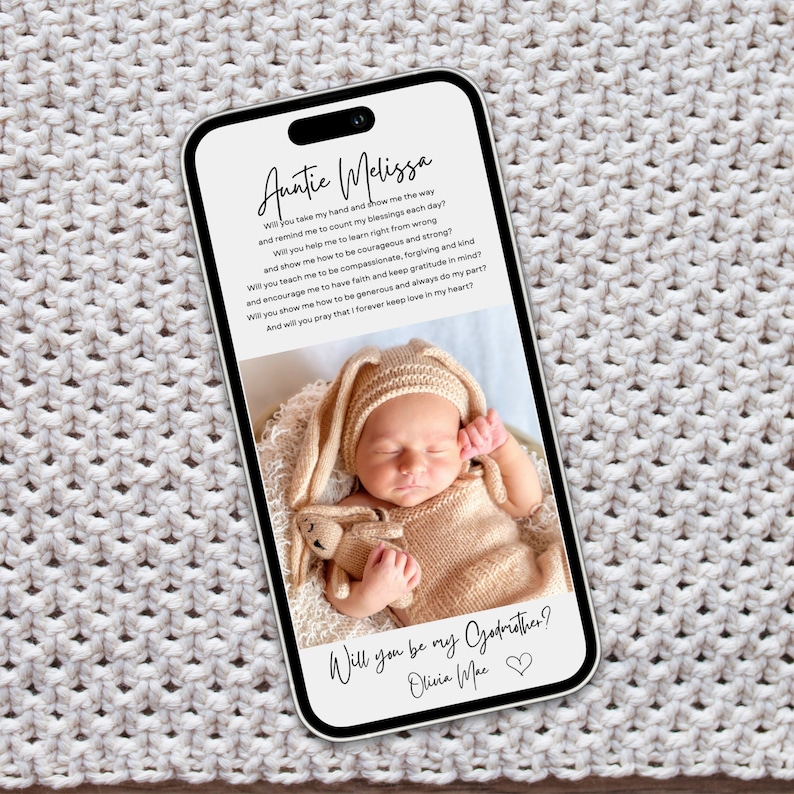 May include: A smartphone screen shows a baby in a bunny outfit and a poem addressed to "Auntie Melissa". The text asks "Will you be my Godmother? Olivia Mae". The phone is on a cream-colored knitted surface.