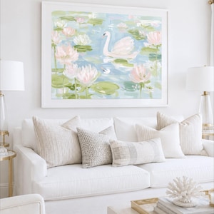 May include: A framed wall art print featuring an impressionistic painting of a white swan swimming in a pond filled with light pink and white water lilies, green lily pads, and soft blue water, displayed in a white frame above a white sofa.
