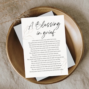 May include: A white ceramic mug with a black handle and the text "But First, Coffee" in a bold, black font. The mug is set against a blurred background, suggesting a cozy setting.
