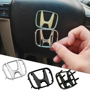 May include: A collection of Honda car emblem replacements. The image shows a chrome emblem being held, with a mounted emblem on a steering wheel. Additional emblems are displayed in silver, black, and a black frame.