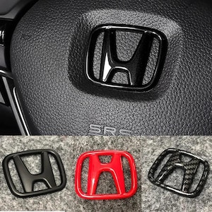 Puede incluir: Emblema negro de Honda sobre una superficie negra texturizada, con tres emblemas adicionales en negro, rojo y patrones de fibra de carbono. Los emblemas están diseñados para uso automotriz, probablemente para el volante o el exterior.