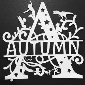 Puede incluir: Recorte de papel blanco con el nombre "AUTUMN", con la letra "A" como elemento principal. La letra est&aacute; adornada con estrellas, un hada, un dinosaurio, un ni&ntilde;o y otros motivos l&uacute;dicos. El fondo es negro.