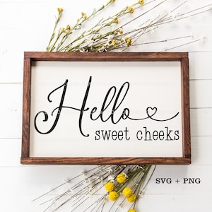 May include: A wooden sign with the text "Hello sweet cheeks" in black cursive font with a small heart symbol. The sign is surrounded by dried flowers with white and yellow blooms.