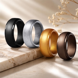 May include: A set of four smooth, rounded rings in matte black, metallic silver, metallic gold, and dark bronze. Each ring features a simple, solid band design with a consistent width and a clean, uniform finish across the entire surface.