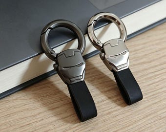 May include: Two keychains featuring a metallic Iron Man helmet design attached to a circular spring-loaded clasp and a black leather strap. One keychain has a dark gunmetal finish, while the other has a polished silver-tone metallic finish.