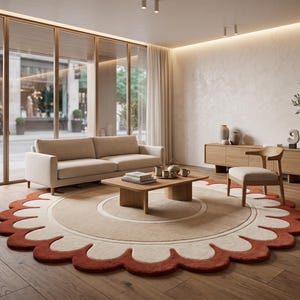 May include: A large circular area rug featuring a central beige circle surrounded by a cream-coloured ring and a scalloped outer border in a deep terracotta orange. The rug is placed on a wooden floor in a room with a sofa, coffee table, and chair.