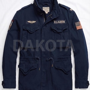 May include: A navy blue field jacket featuring a high collar, four front pockets with flaps, and a drawstring waist. The chest displays a gold-tone wing emblem and a R.LAUREN patch. An American flag patch is on the left sleeve and a graphic patch on the right.