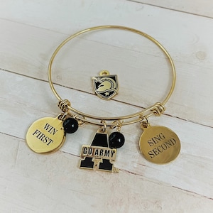 May include: Gold-toned bangle bracelet with multiple charms. Charms include a shield, two round charms with text, and a charm with the words "GO ARMY". The bracelet also has black beads.