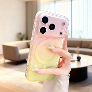Op de afbeelding: Een doorzichtige telefoonhoes met een kleurovergang, van roze naar geel. De hoes heeft een cirkelvormig ontwerp op de achterkant en een doorzichtige rand. De telefoonhoes heeft drie cameralenzen en een flitser.
