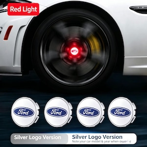 Puede incluir: Cuatro tapacubos circulares blancos con el logotipo azul de Ford. La imagen muestra una rueda de coche en movimiento con una luz roja brillante en el centro. El texto en la imagen incluye Red Light, Silver Logo Version y Note your car model.