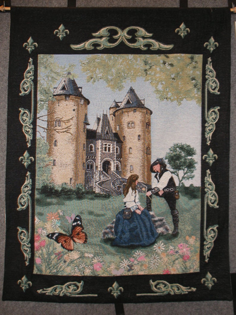 Puede incluir: Un tapiz que representa un castillo medieval con una pareja de pie frente a &eacute;l. El castillo est&aacute; hecho de piedra y tiene una torre alta. La pareja est&aacute; vestida con ropa medieval. El tapiz est&aacute; enmarcado en un marco negro con detalles ornamentados.
