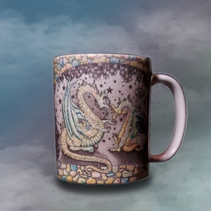 May include: A white ceramic mug with a colorful design of two dragons with stars and a stone-like pattern around the rim.