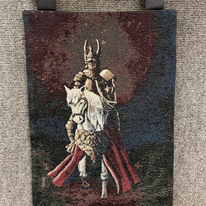 May include: A tapestry wall hanging featuring a knight in armor riding a white horse. The knight is wearing a red cape and a helmet with a plume. The background is a dark blue with a red moon.