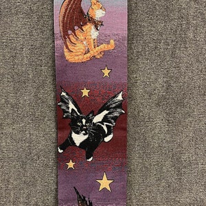 May include: A tapestry wall hanging with a purple, blue, and red background. Three cats with wings are flying against a starry night sky. The cats are orange, black and white, and brown and white.