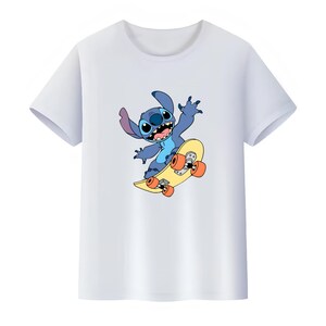 K&ouml;nnte beinhalten: Ein wei&szlig;es T-Shirt mit kurzen &Auml;rmeln und einem Grafikdruck eines blauen Alien-Charakters mit gro&szlig;en Ohren und einem breiten L&auml;cheln, der auf einem gelben Skateboard mit orangefarbenen Rollen f&auml;hrt. Die Figur zeigt sich in einer dynamischen Pose.