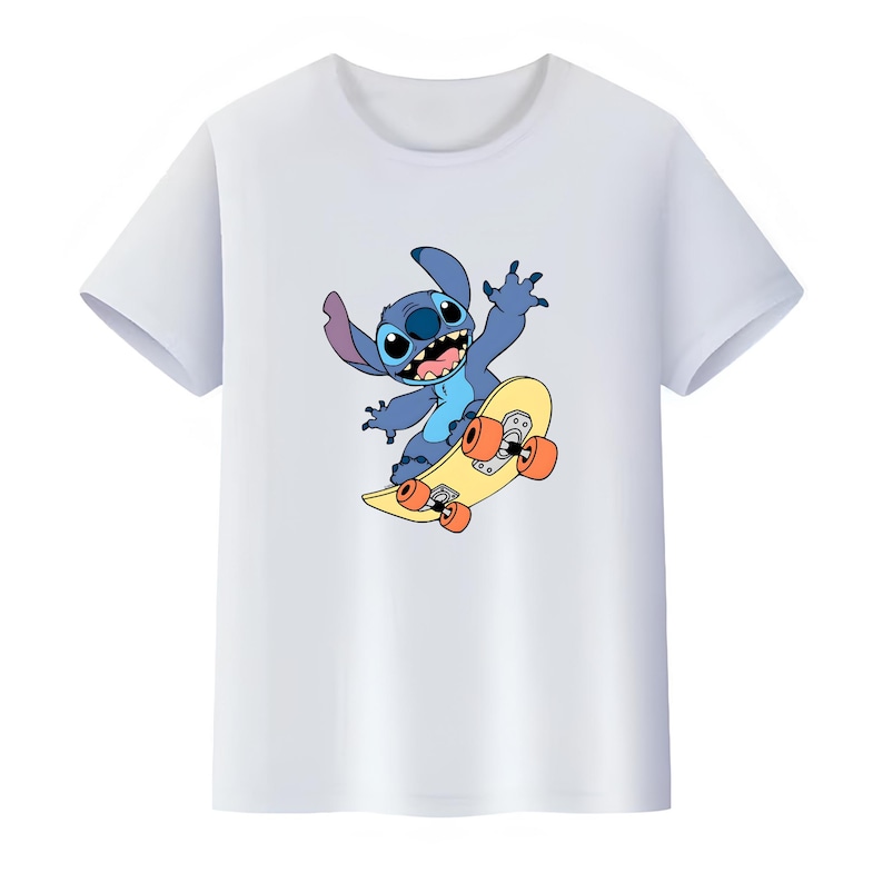 K&ouml;nnte beinhalten: Ein wei&szlig;es T-Shirt mit kurzen &Auml;rmeln und einem Grafikdruck eines blauen Alien-Charakters mit gro&szlig;en Ohren und einem breiten L&auml;cheln, der auf einem gelben Skateboard mit orangefarbenen Rollen f&auml;hrt. Die Figur zeigt sich in einer dynamischen Pose.
