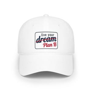 Op de afbeelding: Witte baseballpet met een gebogen klep. De pet heeft een rechthoekige patch met de tekst "live your dream" doorgestreept en "Plan B" in rood en blauw.