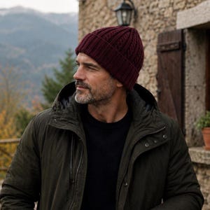 Puede incluir: Un gorro de punto color burdeos intenso con textura acanalada y borde doblado. El gorro está confeccionado con un patrón de punto de ochos vertical que recorre toda la tela, proporcionando una apariencia estructurada y uniforme a este accesorio de invierno.