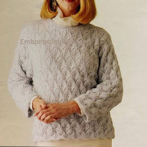 May include: A light blue knitted sweater with a delicate openwork pattern. The sweater has a round neckline and long sleeves.