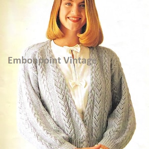 May include: A light blue knitted cardigan with a cable knit pattern and a V-neck. The cardigan has long sleeves and buttons down the front.