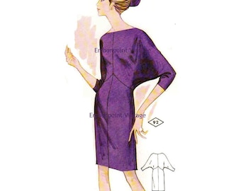 May include: Vintage sewing pattern illustration of a woman wearing a purple dress with a boat neck and 3/4 sleeves. The dress has a fitted bodice and a slightly flared skirt. The pattern number 92 is visible in the lower right corner.