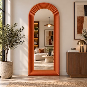 May include: A tall, floor-standing mirror featuring a distinct arched top and a thick, vibrant orange frame with multiple concentric, rounded ridges that create a textured, layered appearance around the reflective glass surface.