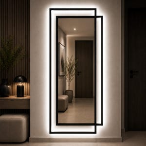 May include: A rectangular wall mirror featuring a black frame with an integrated LED backlight. The design consists of two overlapping rectangular frames that create a layered effect, emitting a bright white glow against the wall surface.