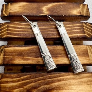 May include: A pair of silver earrings made from repurposed silverware. The earrings are long and rectangular with a textured design.