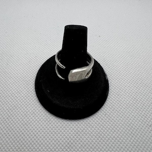 May include: A silver ring with a unique, angular design. The ring is displayed on a black ring holder.